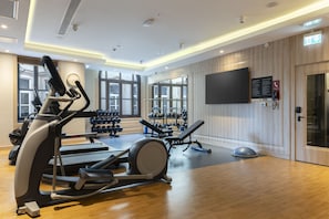 Une salle de sport équipée de machines de cardio, d’un espace dédié à la musculation et d’une grande fenêtre laissant entrer la lumière naturelle.
