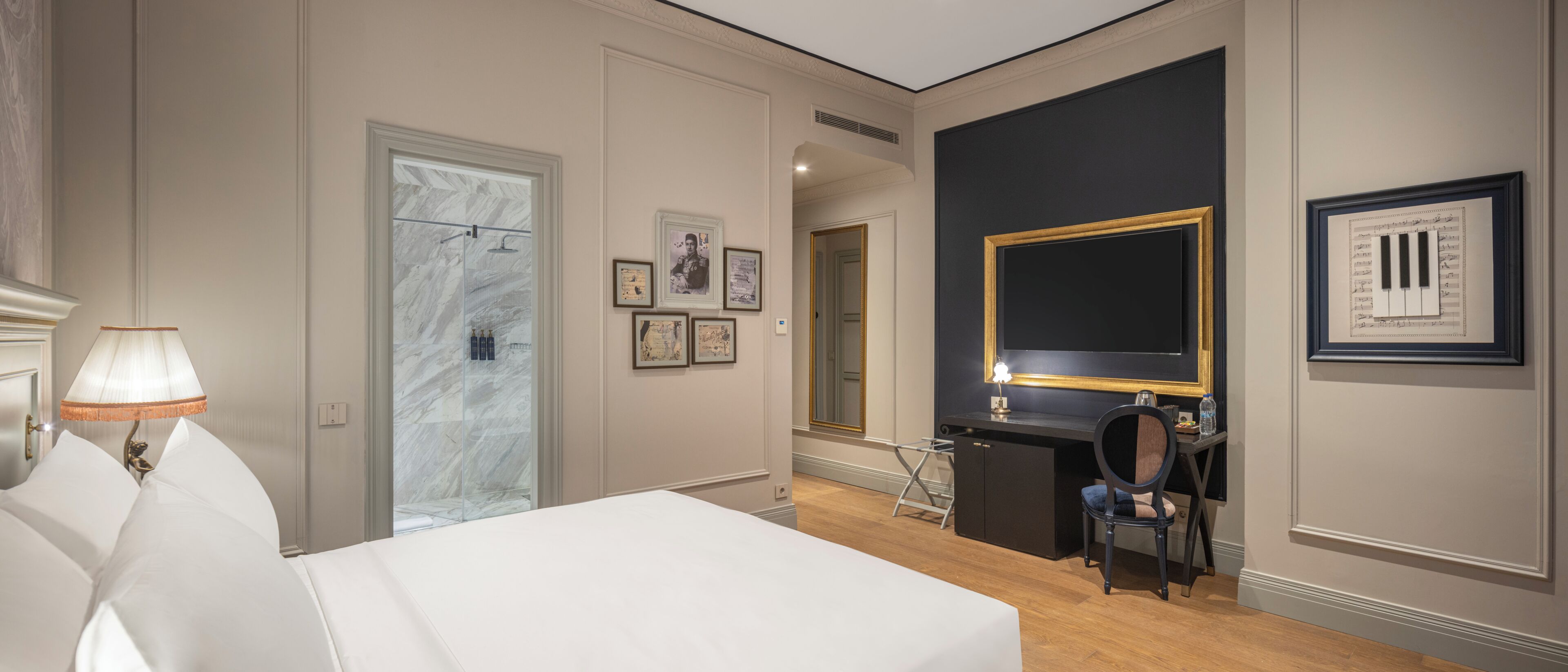 Een hotelkamer met een bed, een bureau, een stoel, een bureaulamp, een spiegel en ingelijste foto's aan de muur.