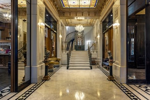 Un vaste hall d’entrée avec un sol en marbre, un escalier et des décorations murales élaborées.