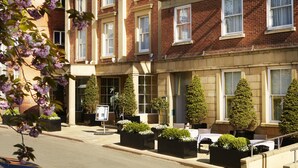 A row of red brick townhouses with white-framed windows, a small outdoor seating area with tables and chairs, and neatly trimmed hedges. - Palm Court Hotel (Scarborough)