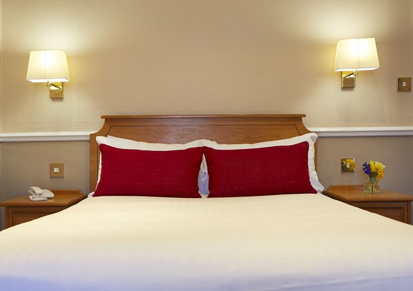 A hotel room with a large bed, two bedside lamps, a nightstand with a telephone, and a small vase with flowers. - Palm Court Hotel (Scarborough)