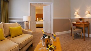 A hotel room with a sofa, a desk, a bed, and a coffee table with a bottle of champagne and glasses. - Palm Court Hotel (Scarborough)