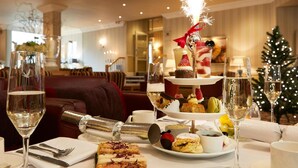 A three-tiered dessert display with a sparkler, surrounded by various pastries and a Christmas tree in the background. - Palm Court Hotel (Scarborough)