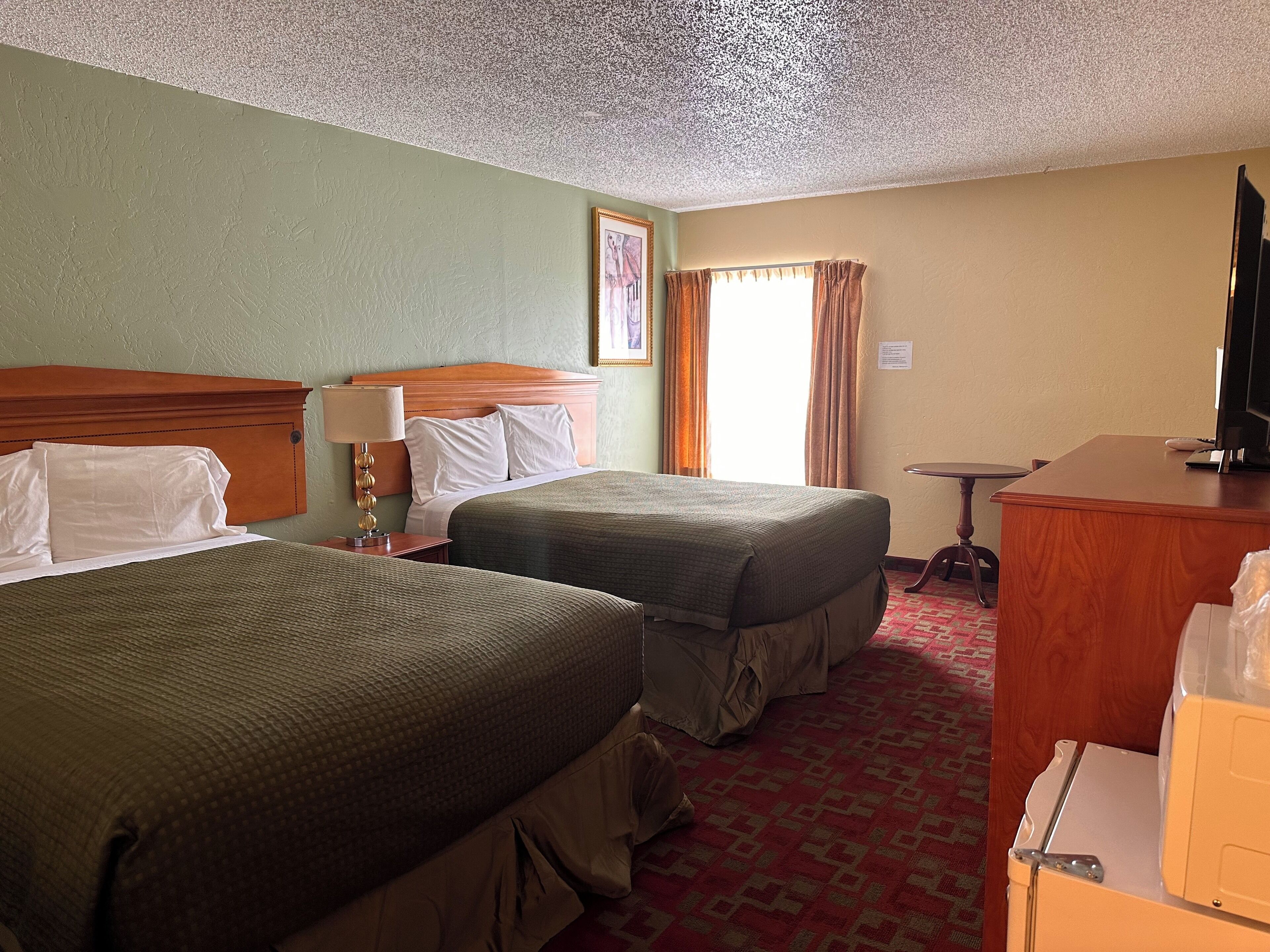 Habitación de hotel con dos camas, un escritorio, un televisor y una ventana con cortinas.