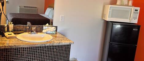 A compact hotel room with a tiled bathroom, a black refrigerator, and a microwave on top.