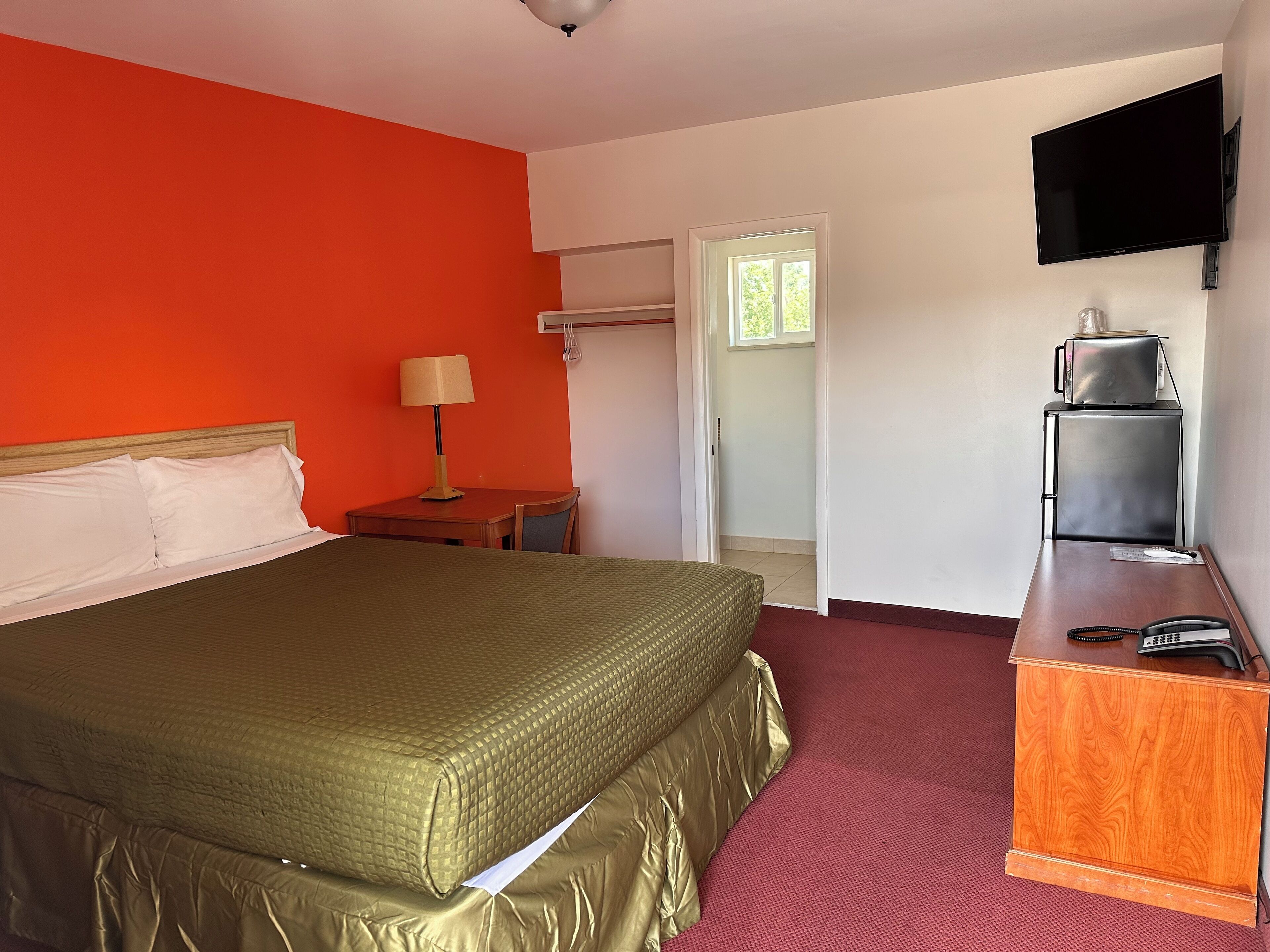 A hotel room with a bed, a desk, a television, and a refrigerator.