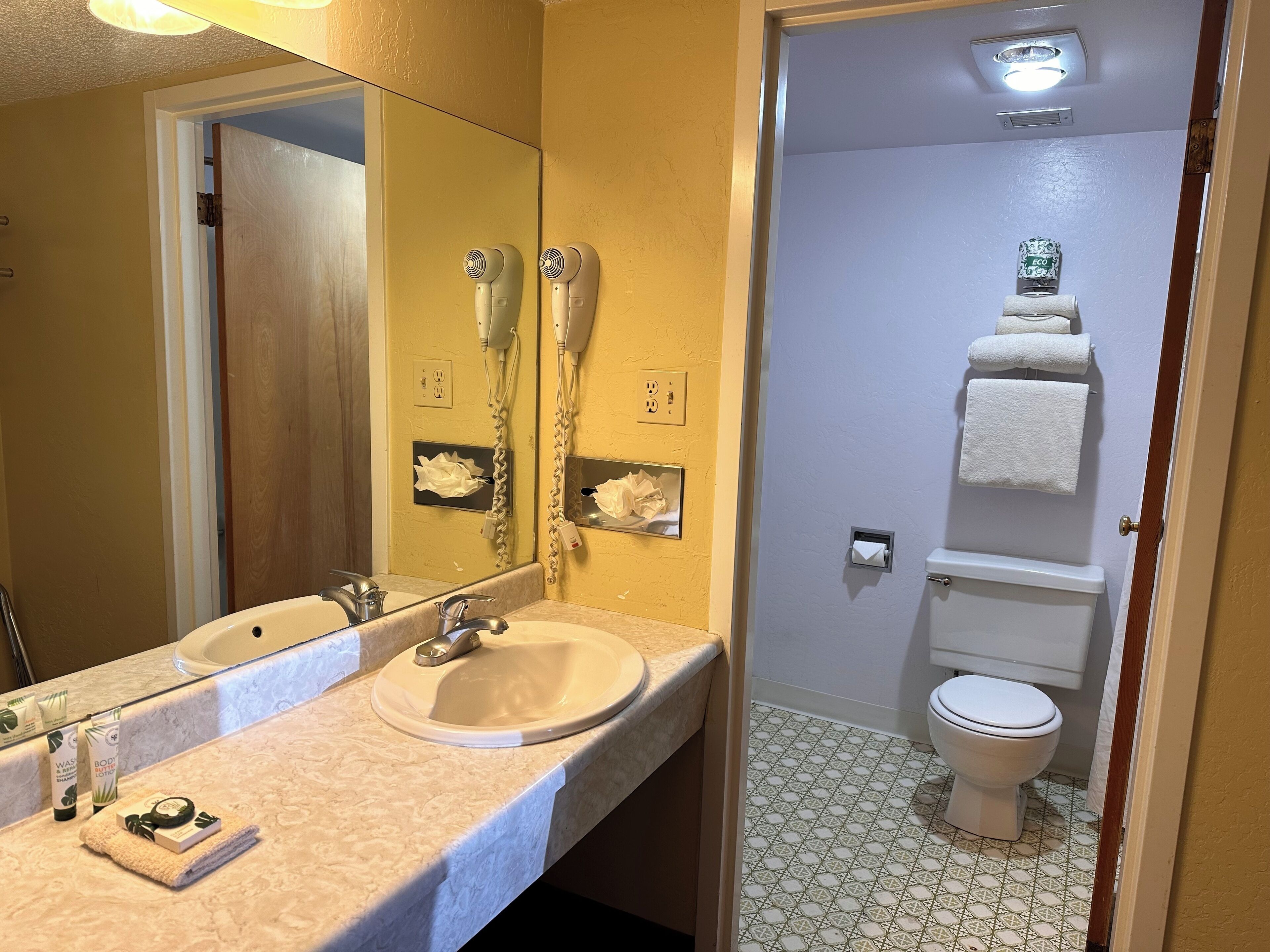 Un baño con lavamanos, dos secadores de pelo, inodoro y espejo.