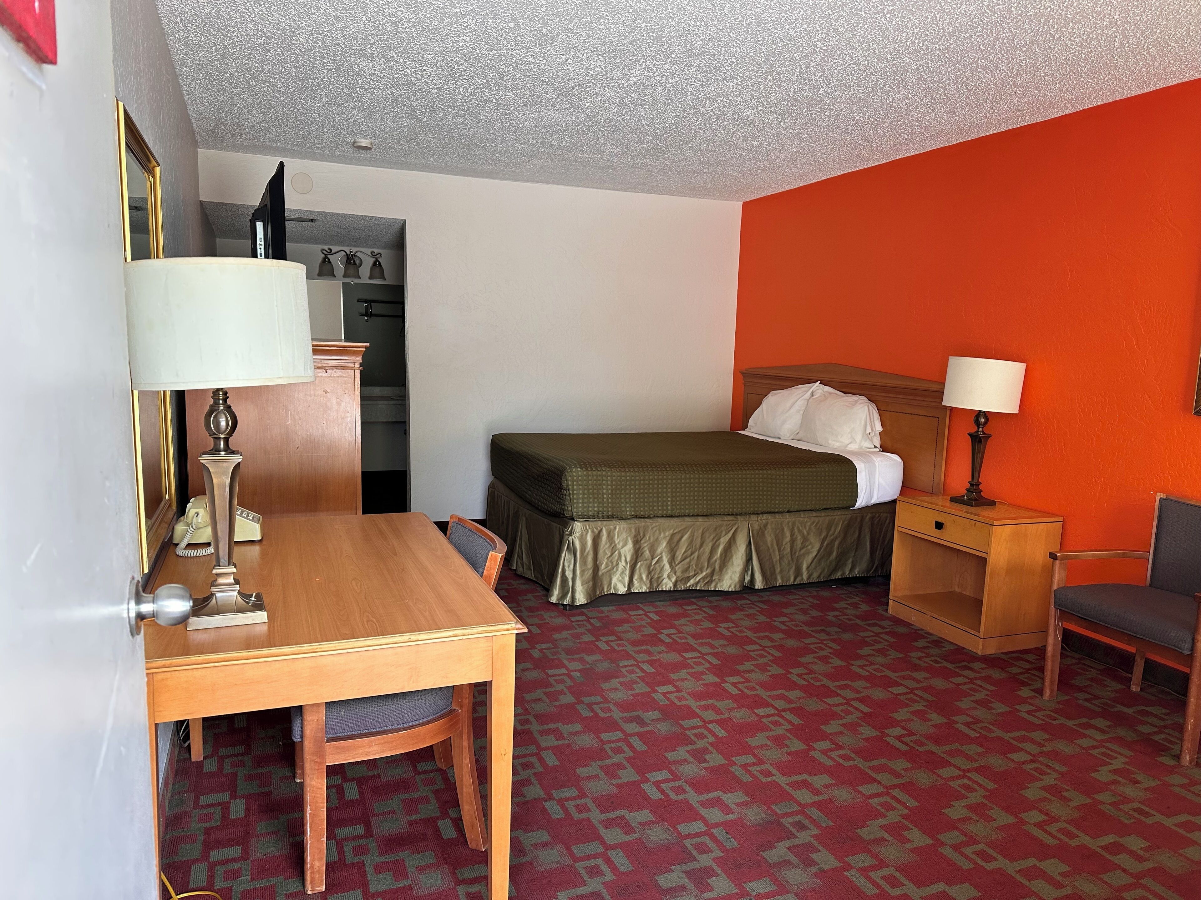 Een hotelkamer met een bed, een bureau, een stoel, een nachtkastje, een lamp en een telefoon.