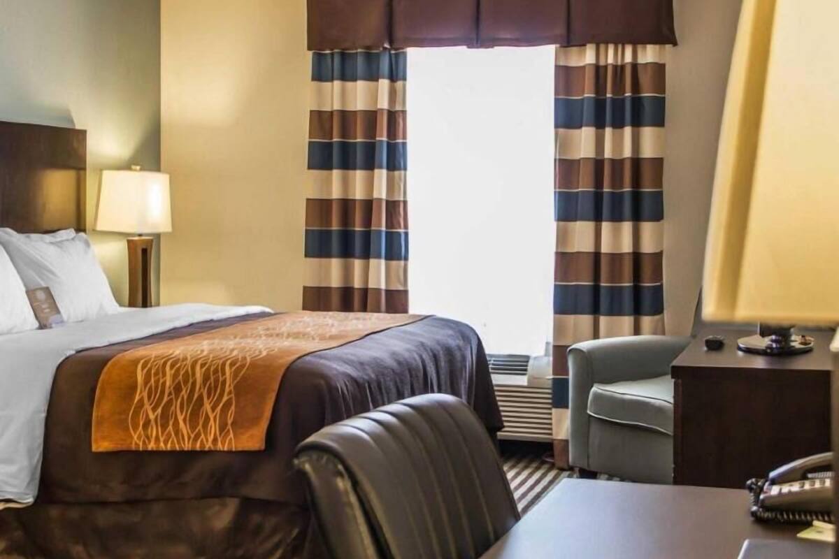 Ein Hotelzimmer mit Bett, Schreibtisch, Stuhl, Lampe und Vorhängen.