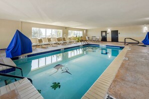 An indoor swimming pool with clear lane markings, lounge chairs, and a lifeguard chair.