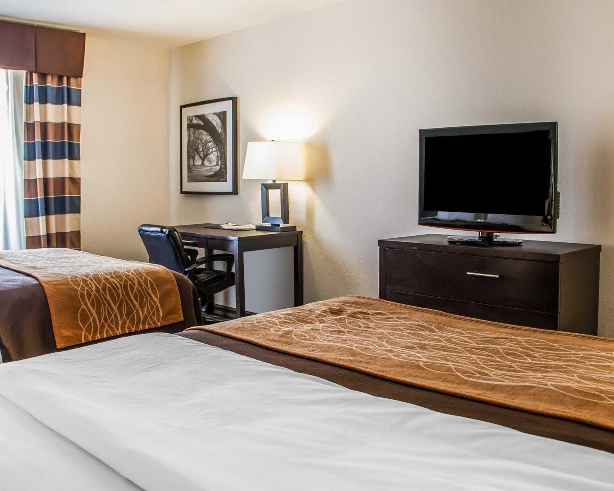 Een hotelkamer met twee bedden, een bureau, een stoel, een televisie en een lamp.