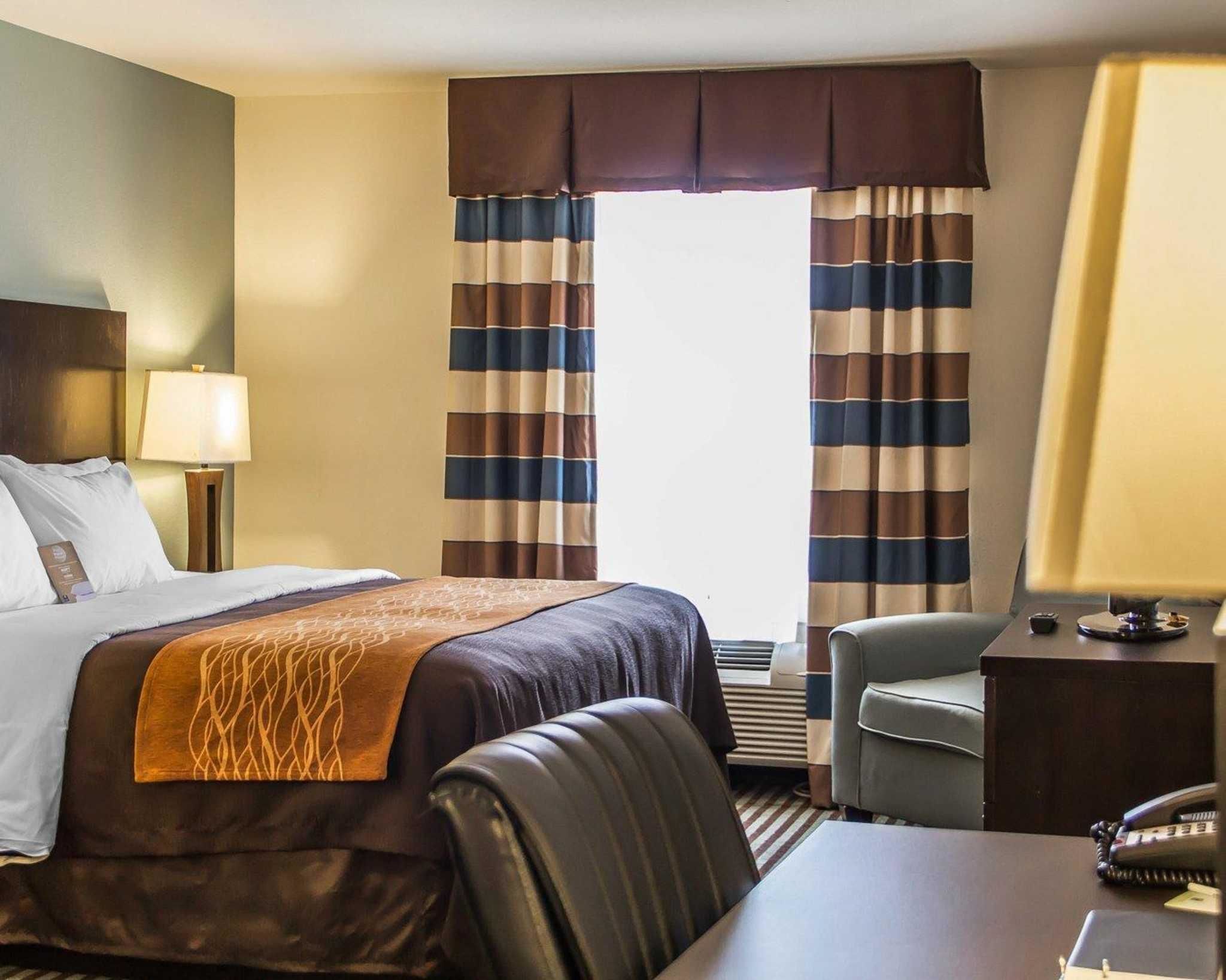 Een hotelkamer met een bed, een bureau, een stoel, een lamp en gordijnen.