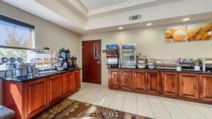 A hotel kitchen with a buffet setup, including a coffee station, a refrigerator, and a beverage dispenser.