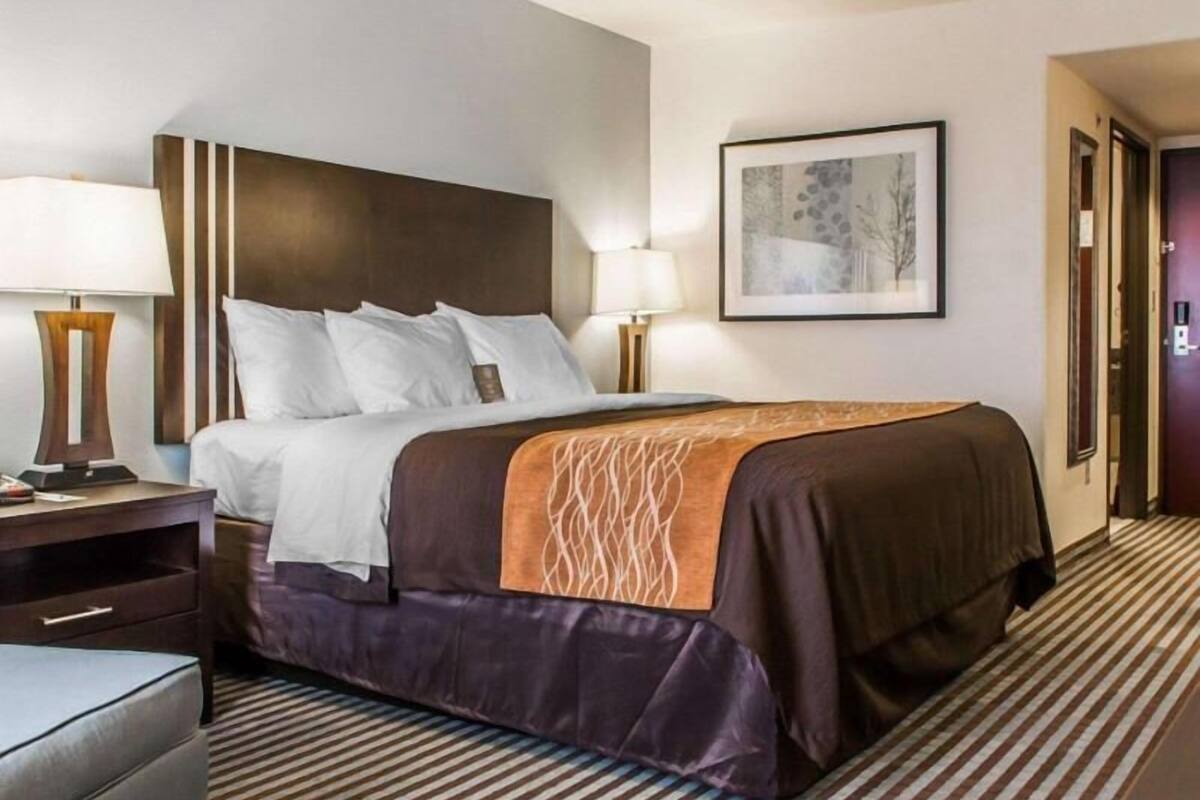 Ein Hotelzimmer mit einem Bett, Nachttischen, einem Sessel, einem gerahmten Bild an der Wand und einem Streifenmuster-Teppich.