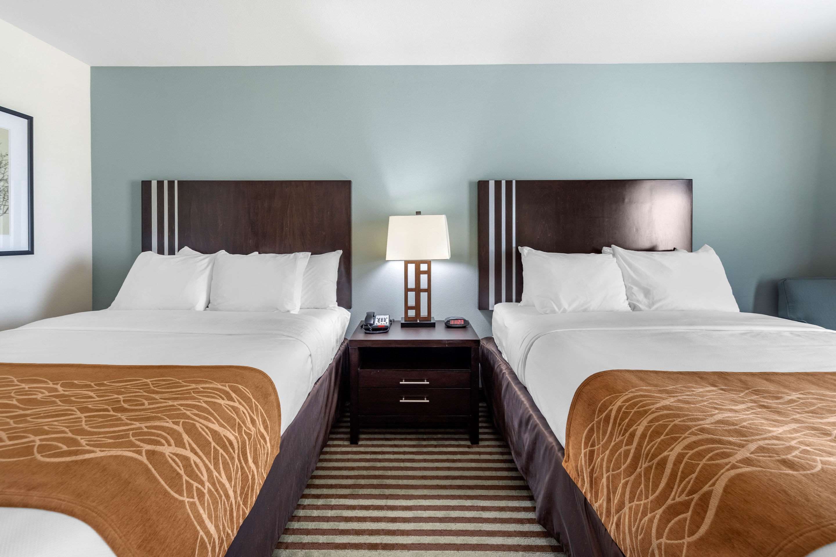A hotel room with two beds, a nightstand with a lamp, and a striped carpet.
