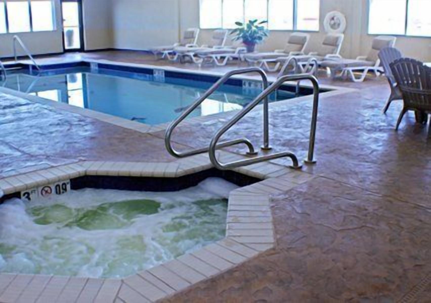 An indoor swimming pool with a hot tub, lounge chairs, and a tiled floor.