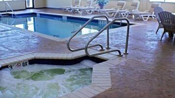 An indoor swimming pool with a hot tub, lounge chairs, and a tiled floor.