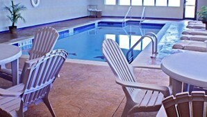 An indoor swimming pool with clear blue water, surrounded by lounge chairs and tables.