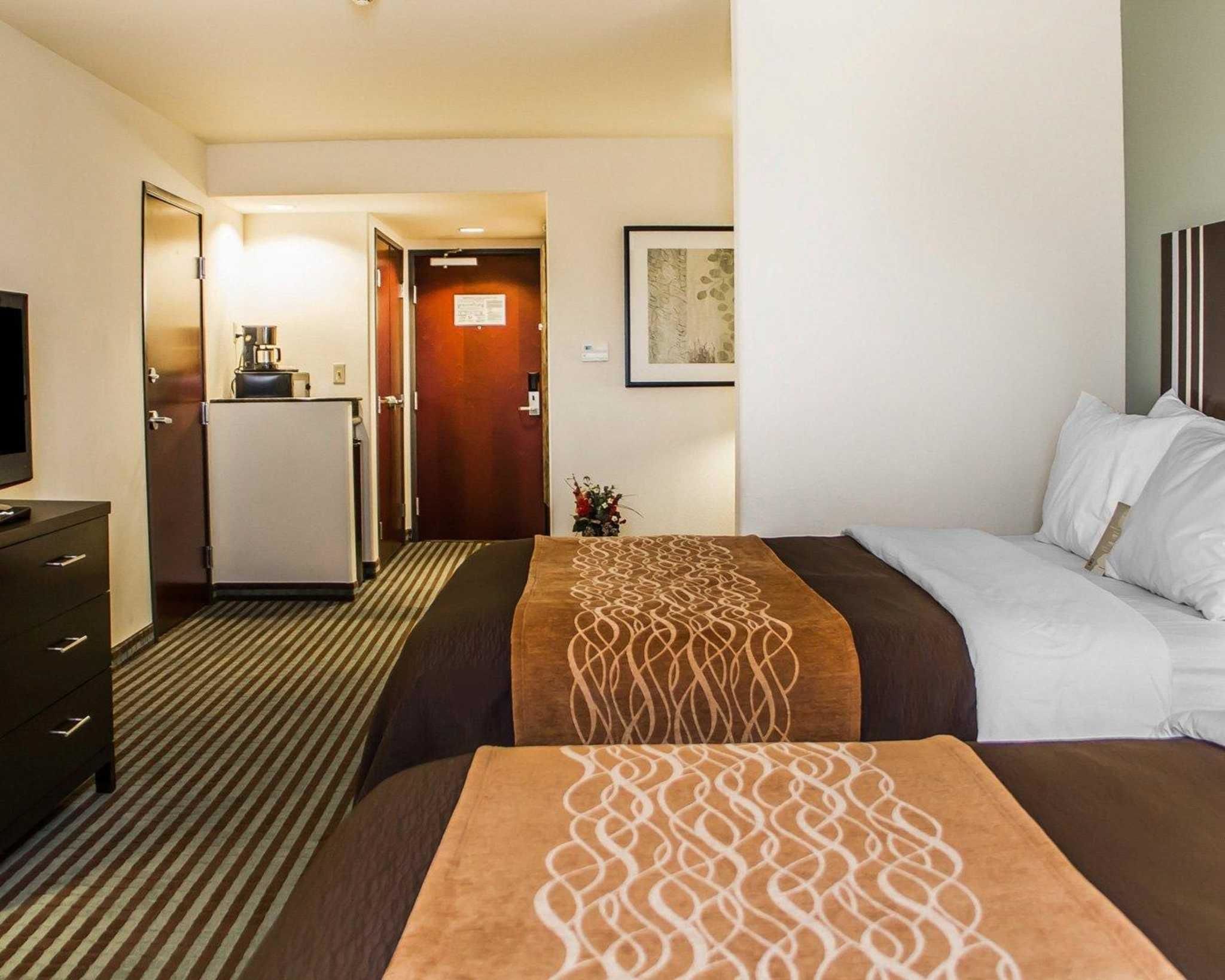A hotel room with two beds, a desk, a refrigerator, and a television.