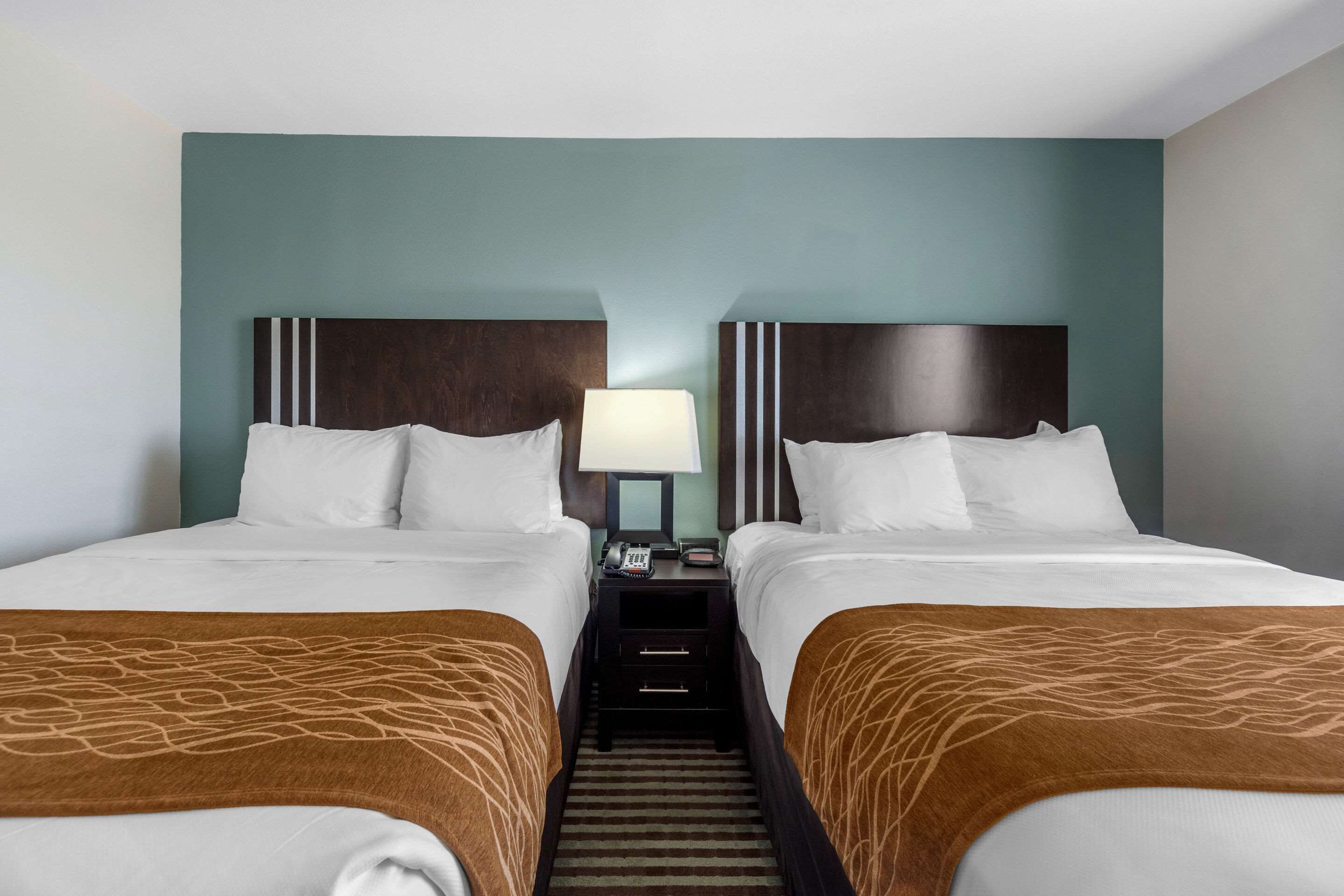 A hotel room with two beds, a nightstand, and a lamp.