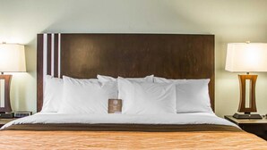 A neatly made bed with white linens and a brown headboard, accompanied by two bedside lamps and a small bedside table with a book.