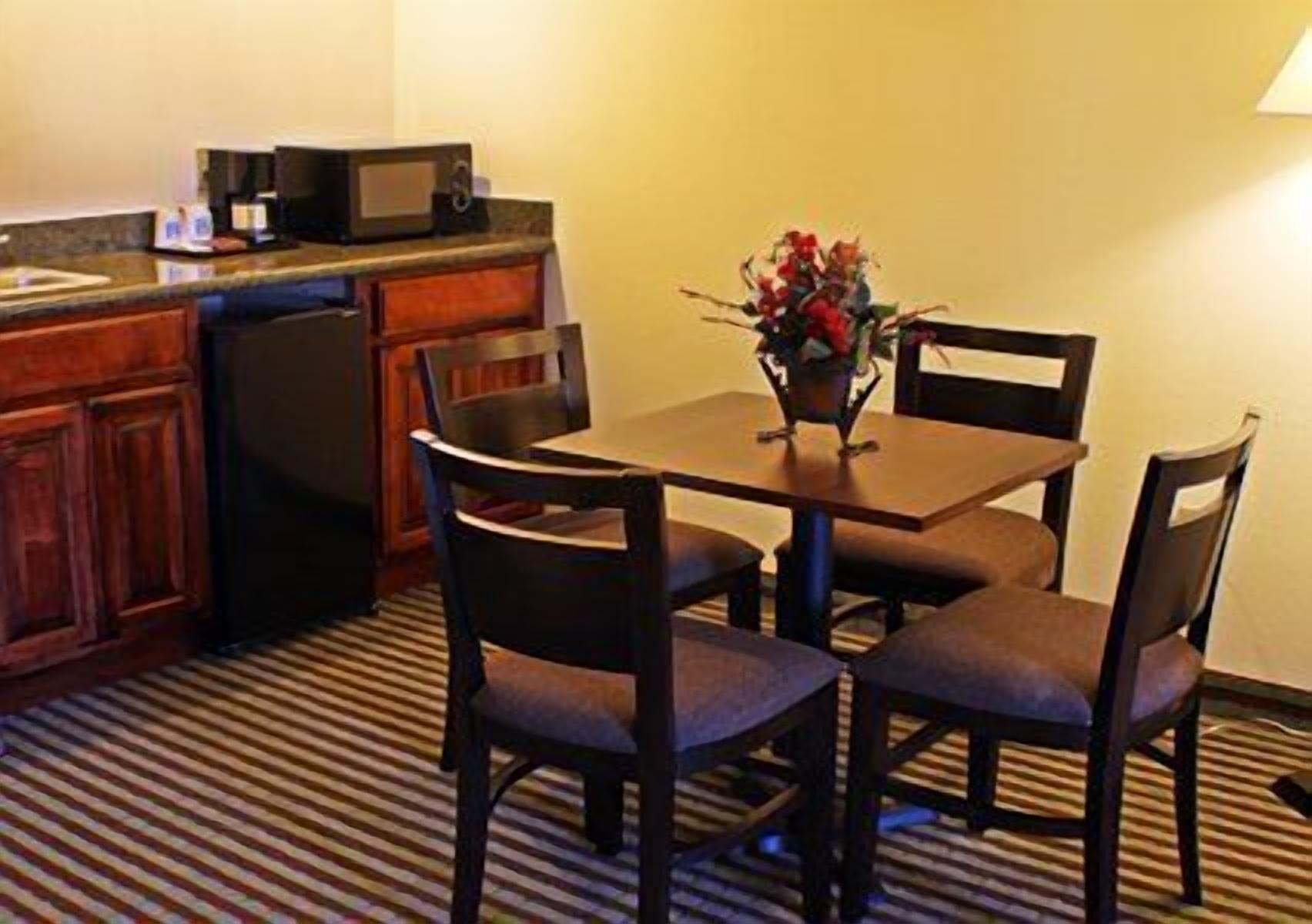 A compact kitchen with a microwave, a coffee maker, and a small dining table with four chairs.