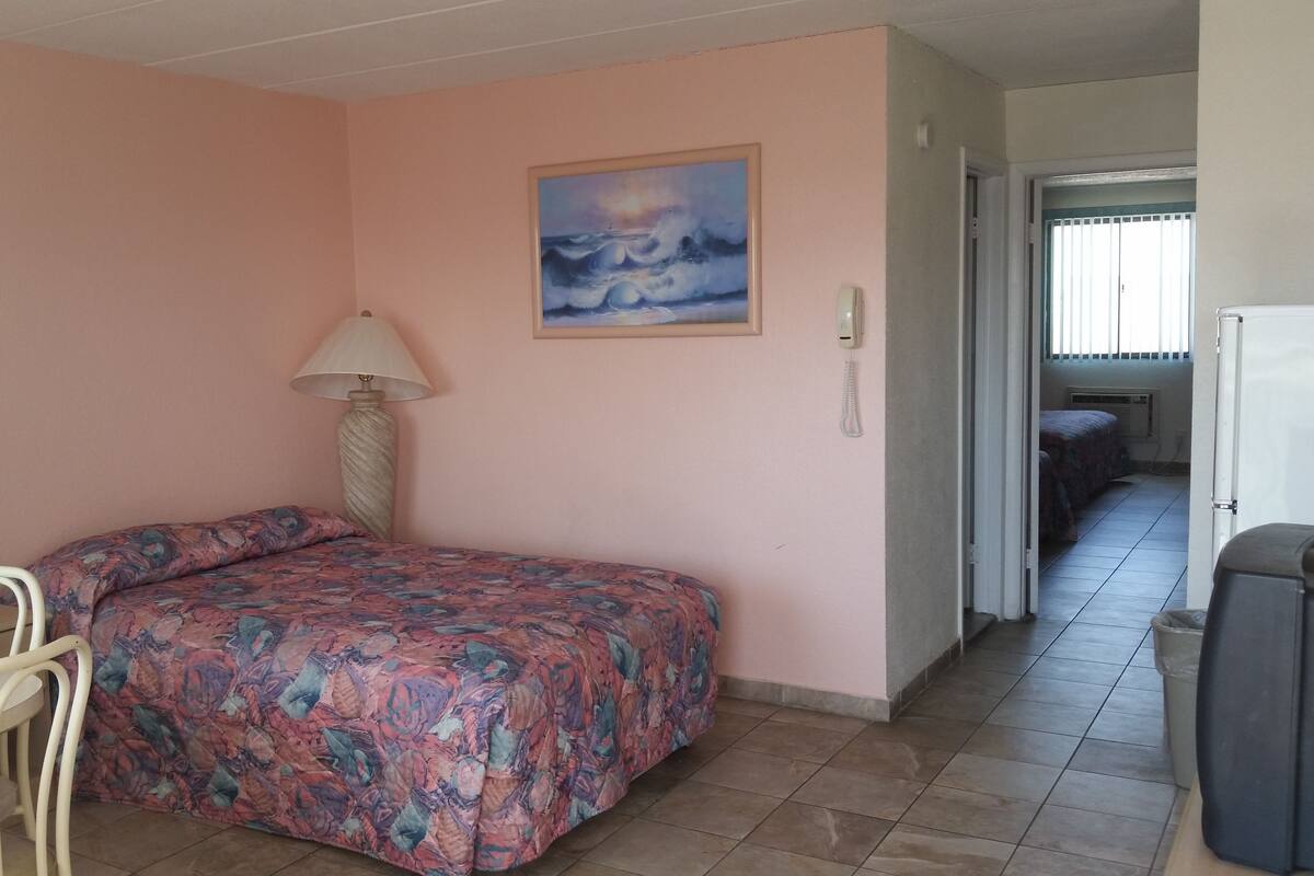 A room with a bed, a desk, a lamp, and a painting on the wall.