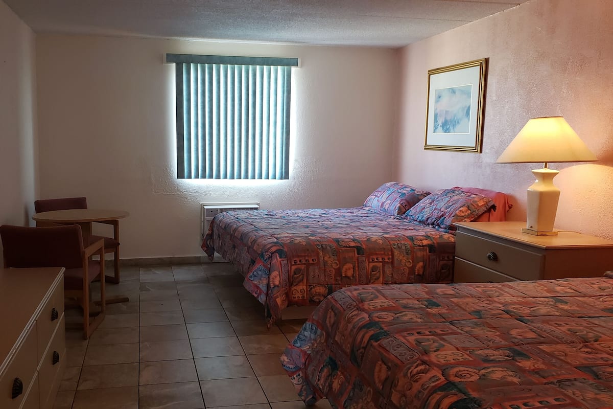 A small, well-lit bedroom with two beds, a desk, and a chair.