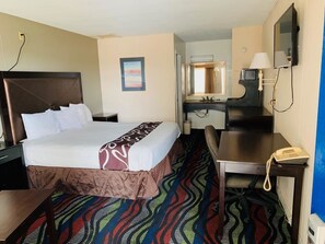 A hotel room with a bed, a desk, a telephone, a mirror, and a bathroom visible through an open door.