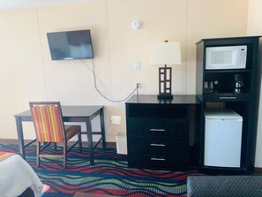 A hotel room with a TV, a desk with a chair, a microwave, a coffee maker, and a refrigerator.