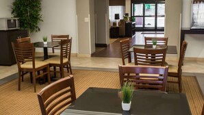 Een restaurantgedeelte in een hotel met houten tafels en stoelen, een kamerplant en een magnetron op een kast.
