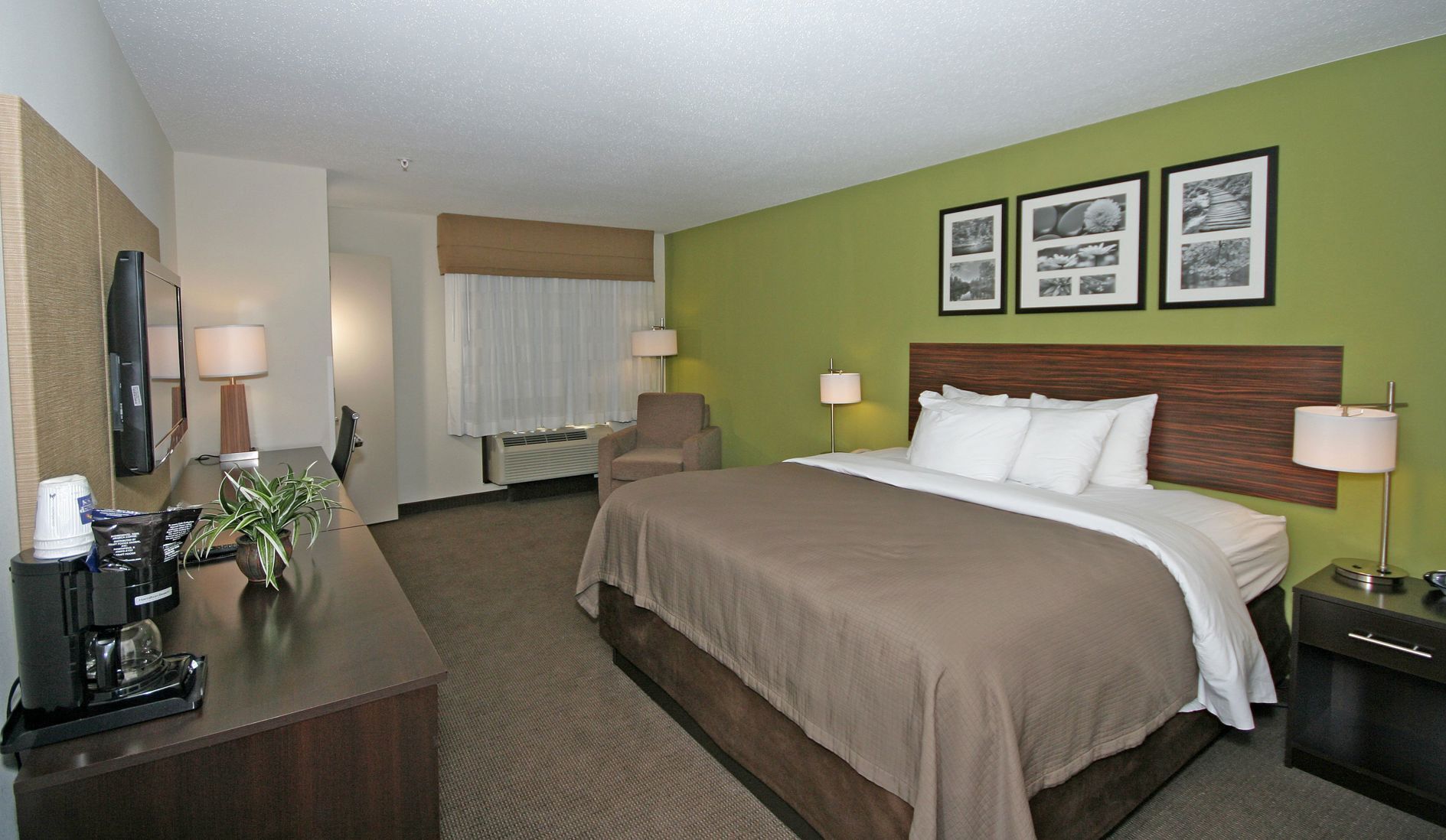 A hotel room with a bed, bedside table, lamp, chair, and a desk with a coffee maker.