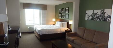 Habitación de hotel con cama, sofá, escritorio y una silla. Se ve una ventana con cortinas y una pared con cuadros enmarcados.