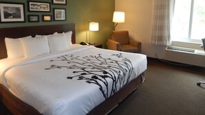 A hotel room with a large bed, a chair, a desk, and a window with curtains. - Sleep Inn & Suites Evergreen I-65 (Evergreen)