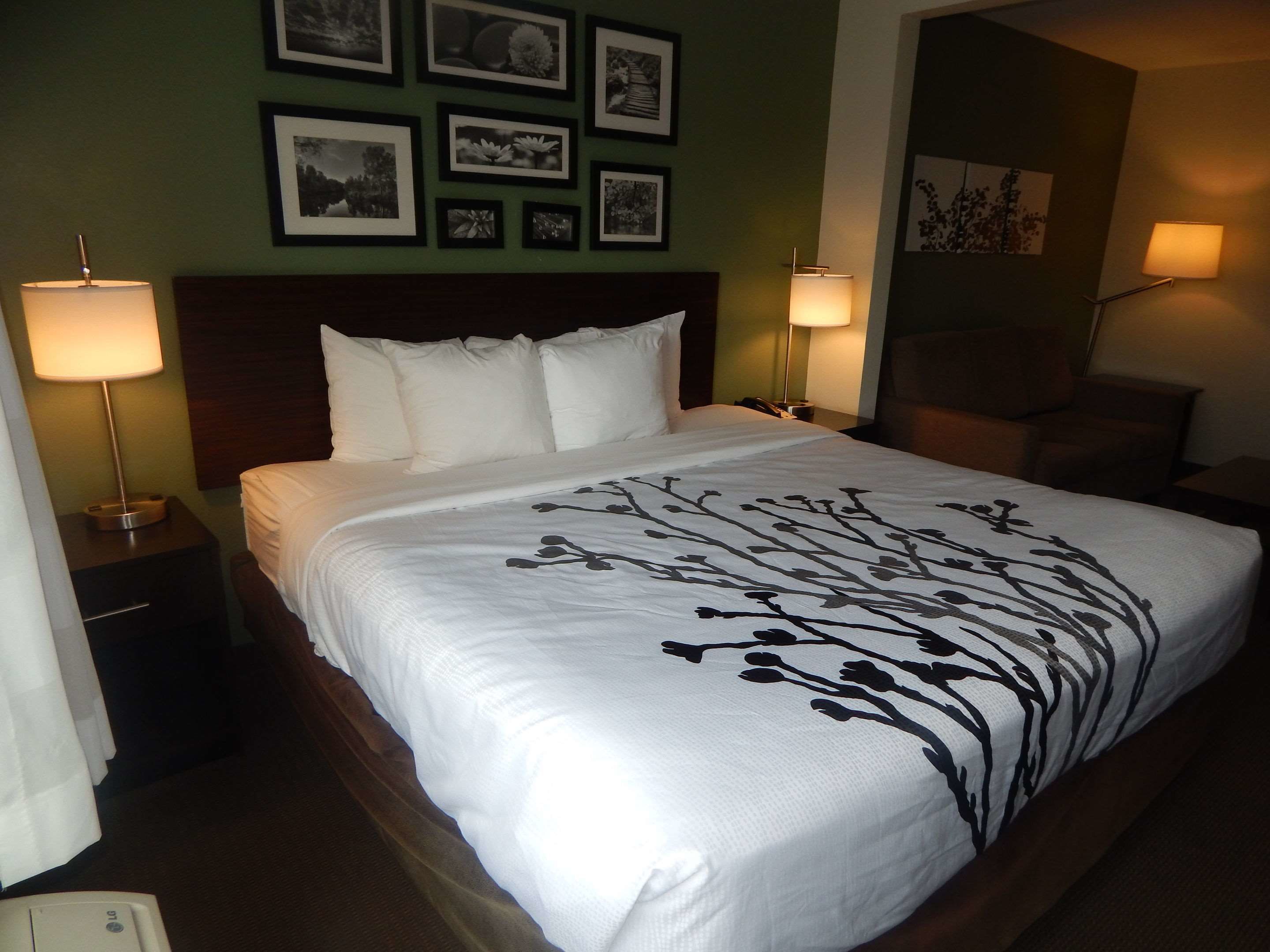 A neatly made bed with a white bedspread and black floral pattern, flanked by two bedside lamps on wooden nightstands.