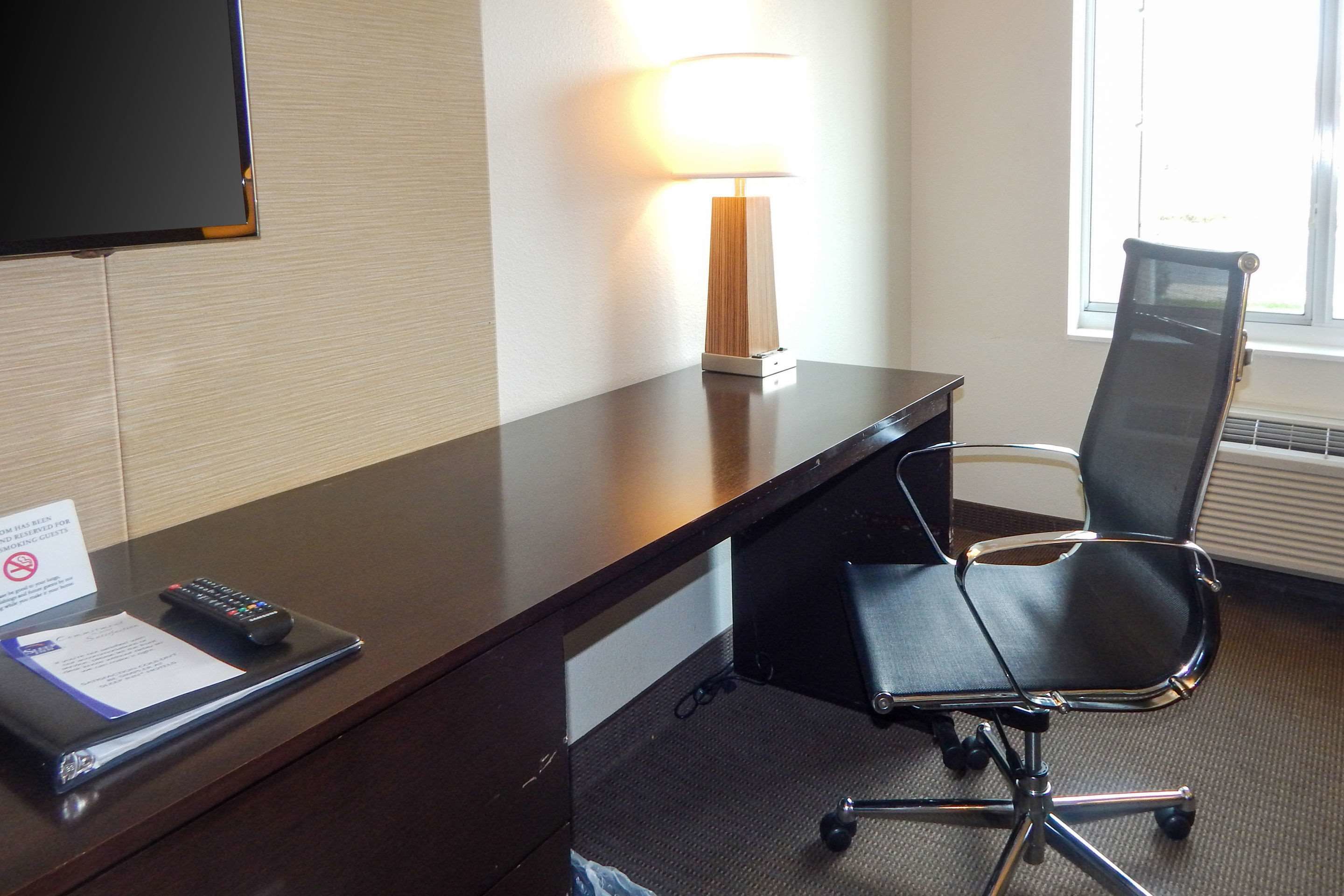 Een hotelkamer met een bureau, een stoel, een lamp, een televisietoestel en een raam.