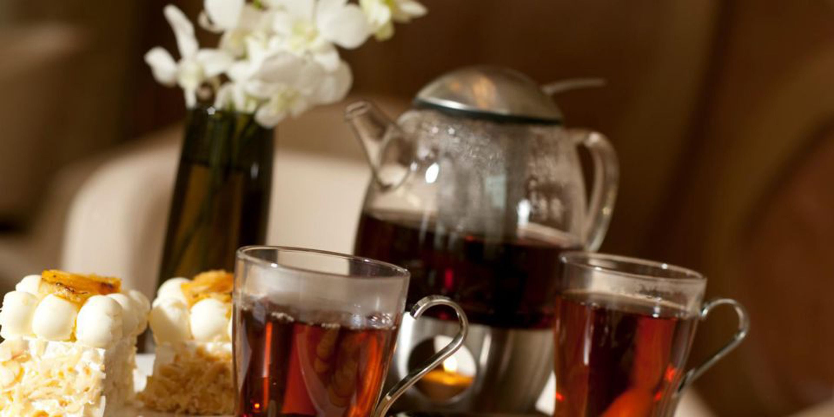 Une table mise avec une théière, deux tasses de thé, un verre d’eau et un dessert.
