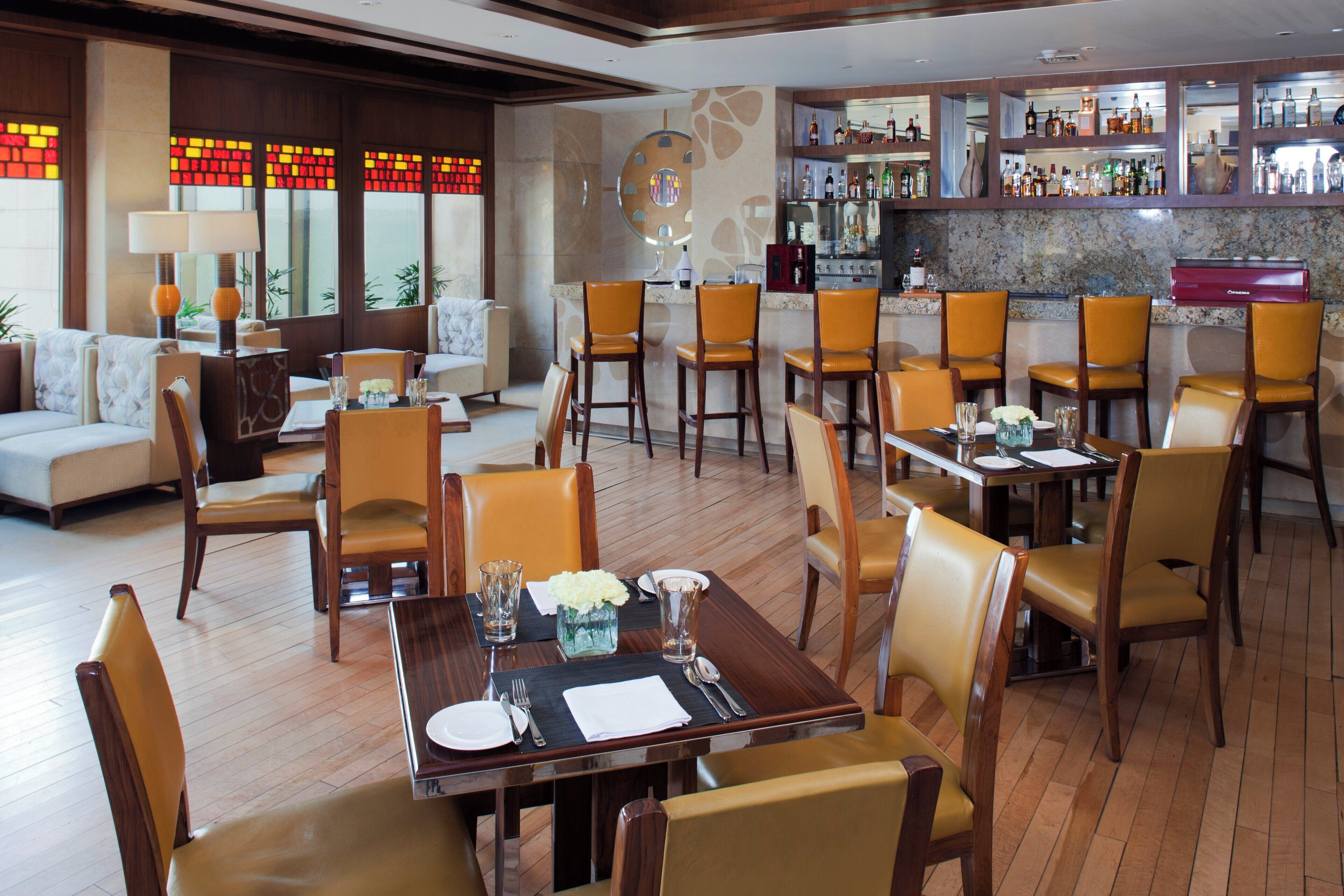 A restaurant with multiple dining tables and chairs, a bar area with various bottles, and a seating area with couches and a coffee table.