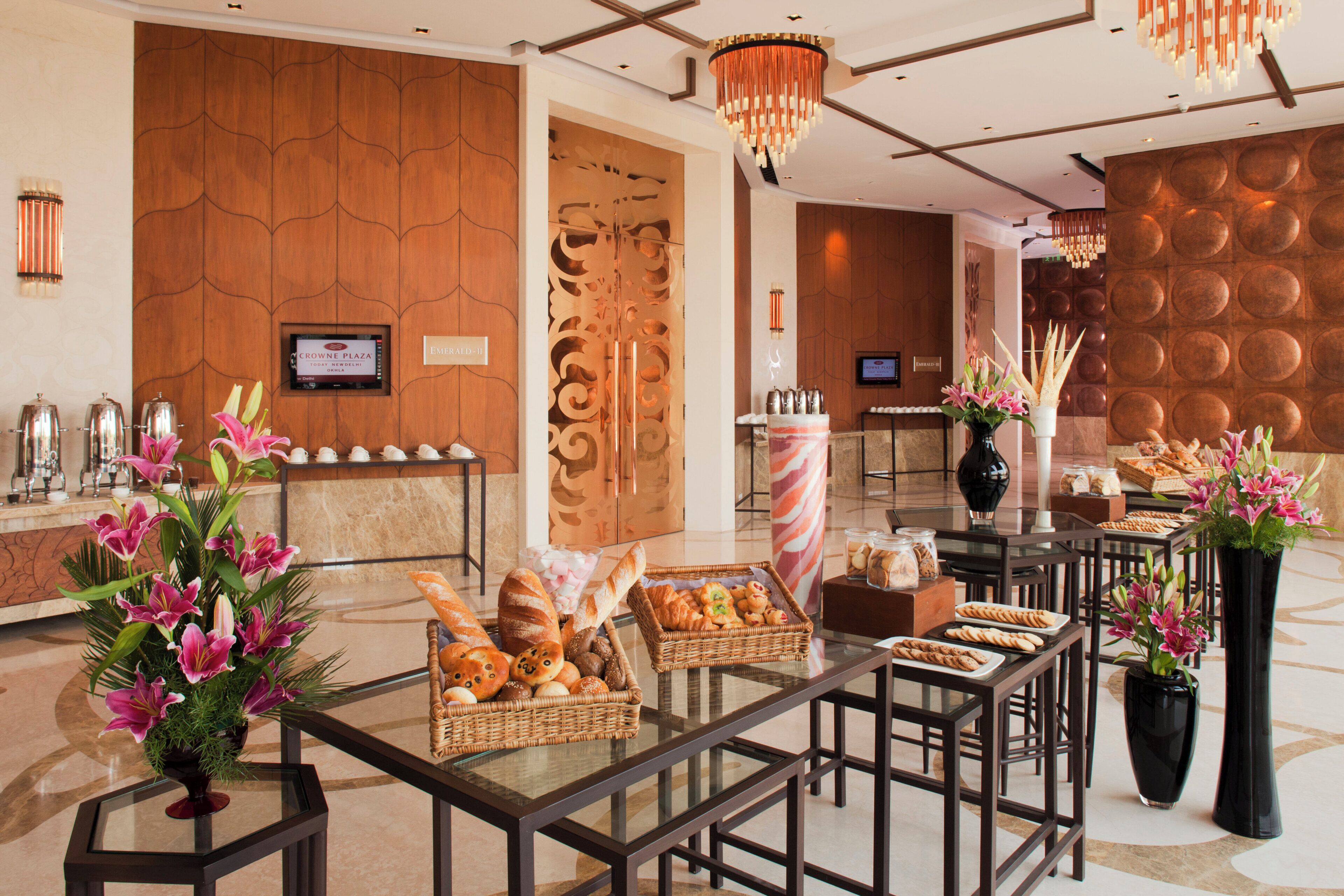 Un hall d’hôtel comprenant un comptoir d’accueil, un espace où l’on peut se servir du café et un buffet proposant diverses pâtisseries et pains.