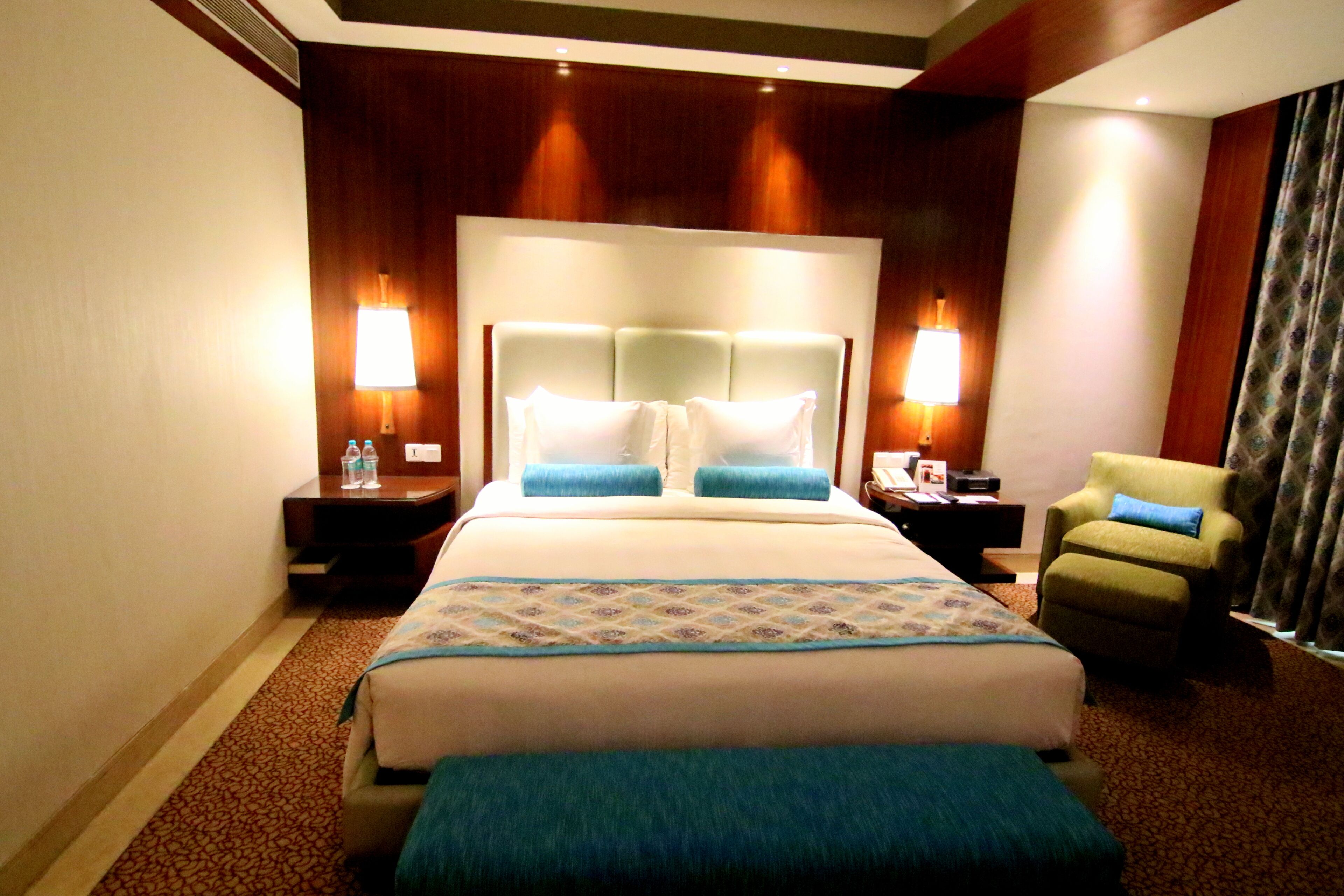 A hotel room with a large bed, two bedside lamps, a chair, and a nightstand.