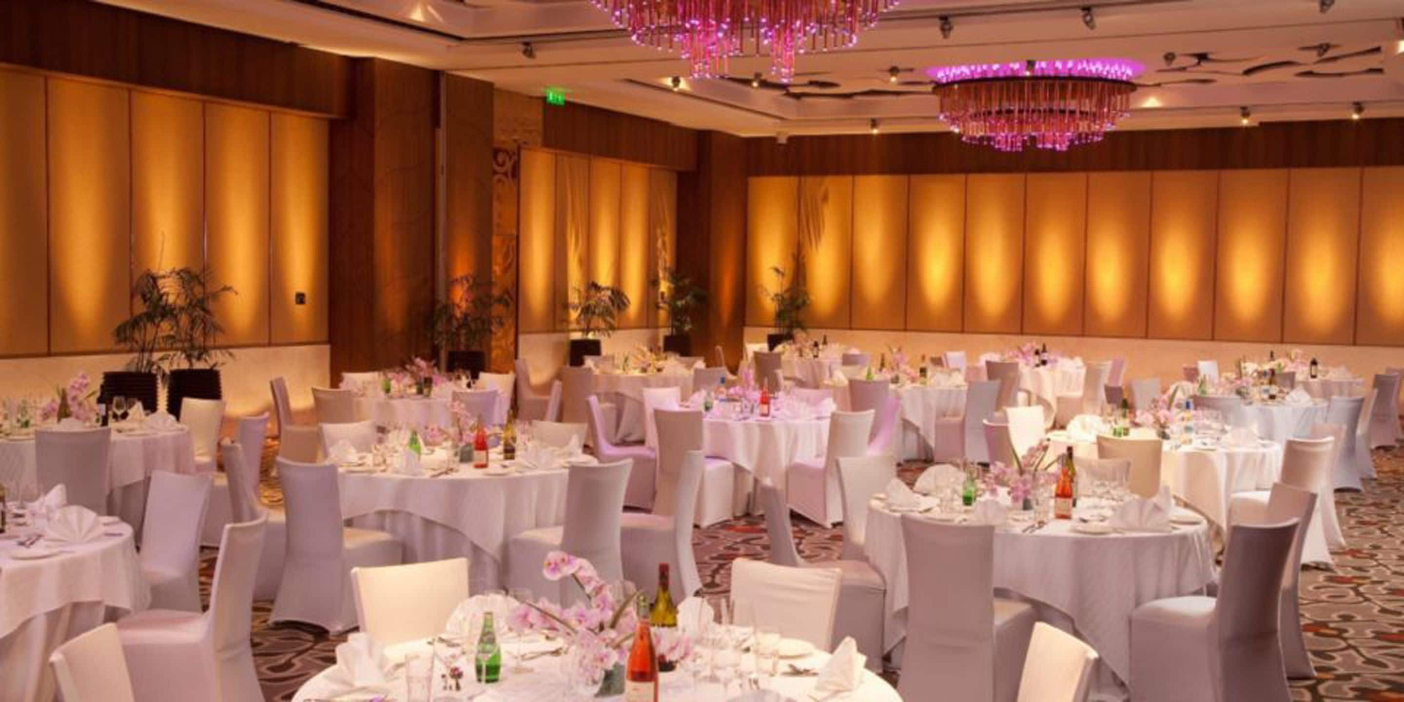 Un salón de banquetes con mesas redondas dispuestas para eventos, con manteles blancos y centros de mesa florales.