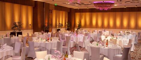 Un salón de banquetes con mesas redondas dispuestas para eventos, con manteles blancos y centros de mesa florales.
