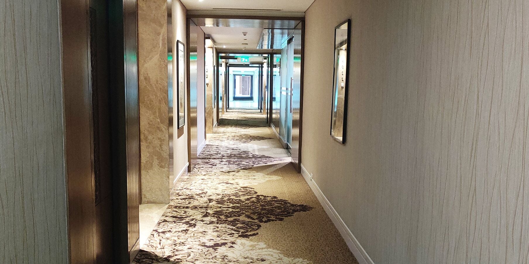 Un pasillo con alfombra estampada, cuadros en las paredes y una puerta espejada.