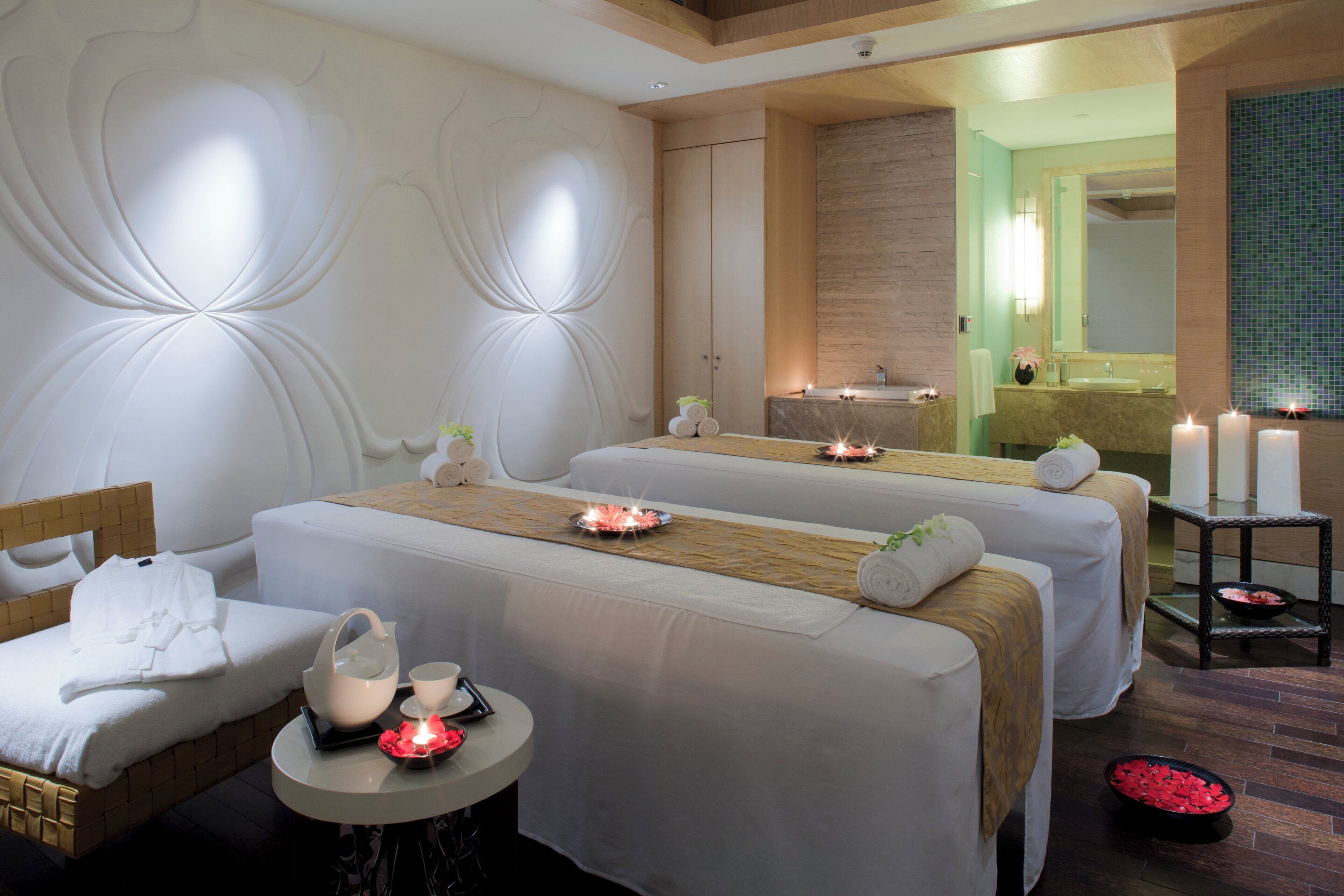 A spa room with two massage tables, a small table with candles, and a mirror.