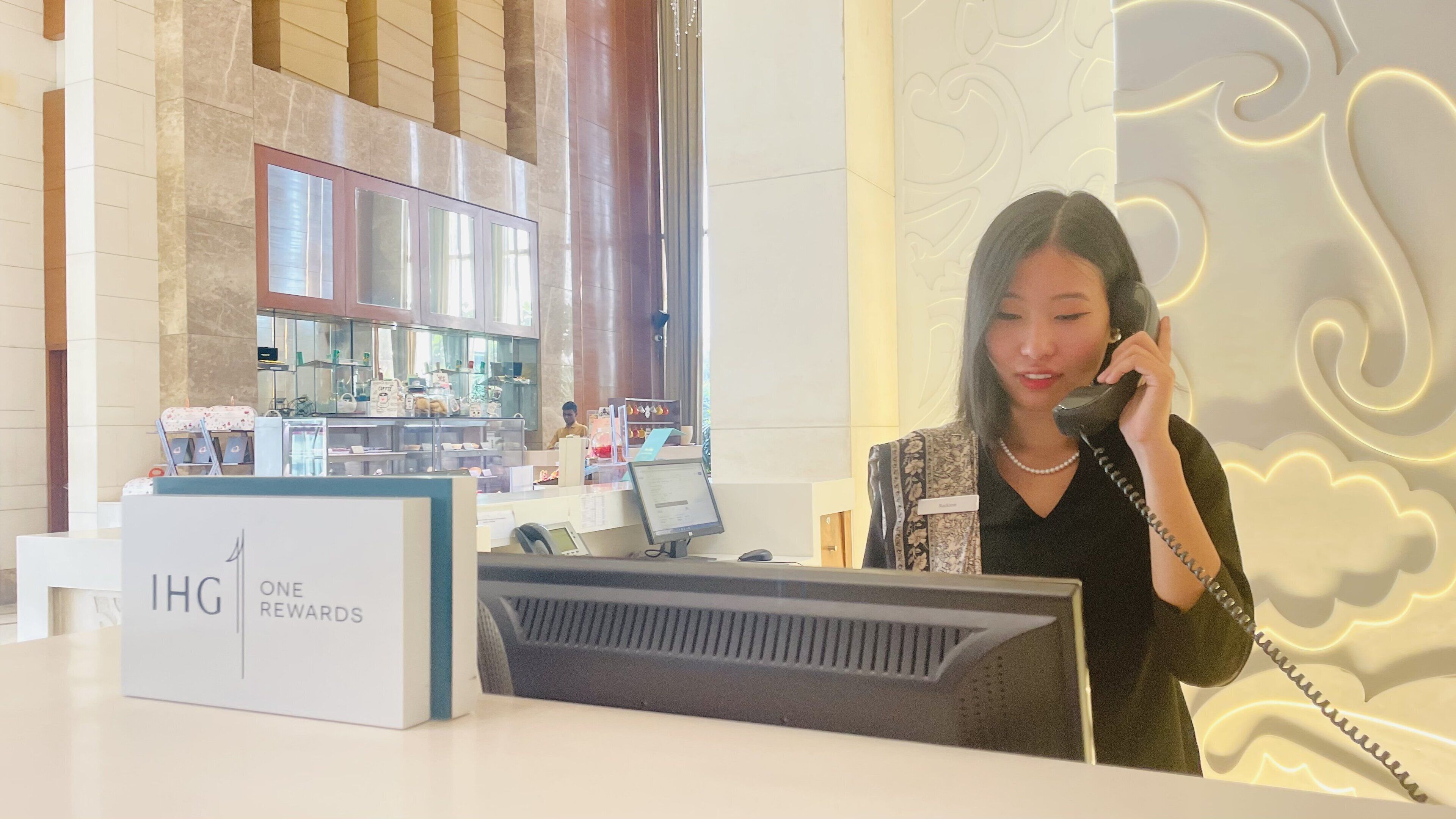 A hotel reception desk with a 'One Rewards' sign, a computer, and a counter with various items.