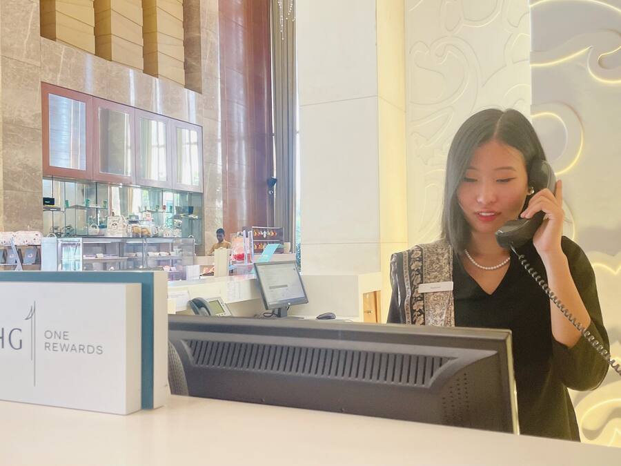 A hotel reception desk with a 'One Rewards' sign, a computer, and a counter with various items.