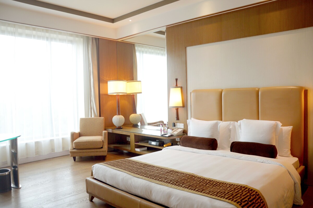 Une chambre d’hôtel avec un grand lit, un bureau avec une lampe, une chaise et une vue sur l’extérieur par la fenêtre.