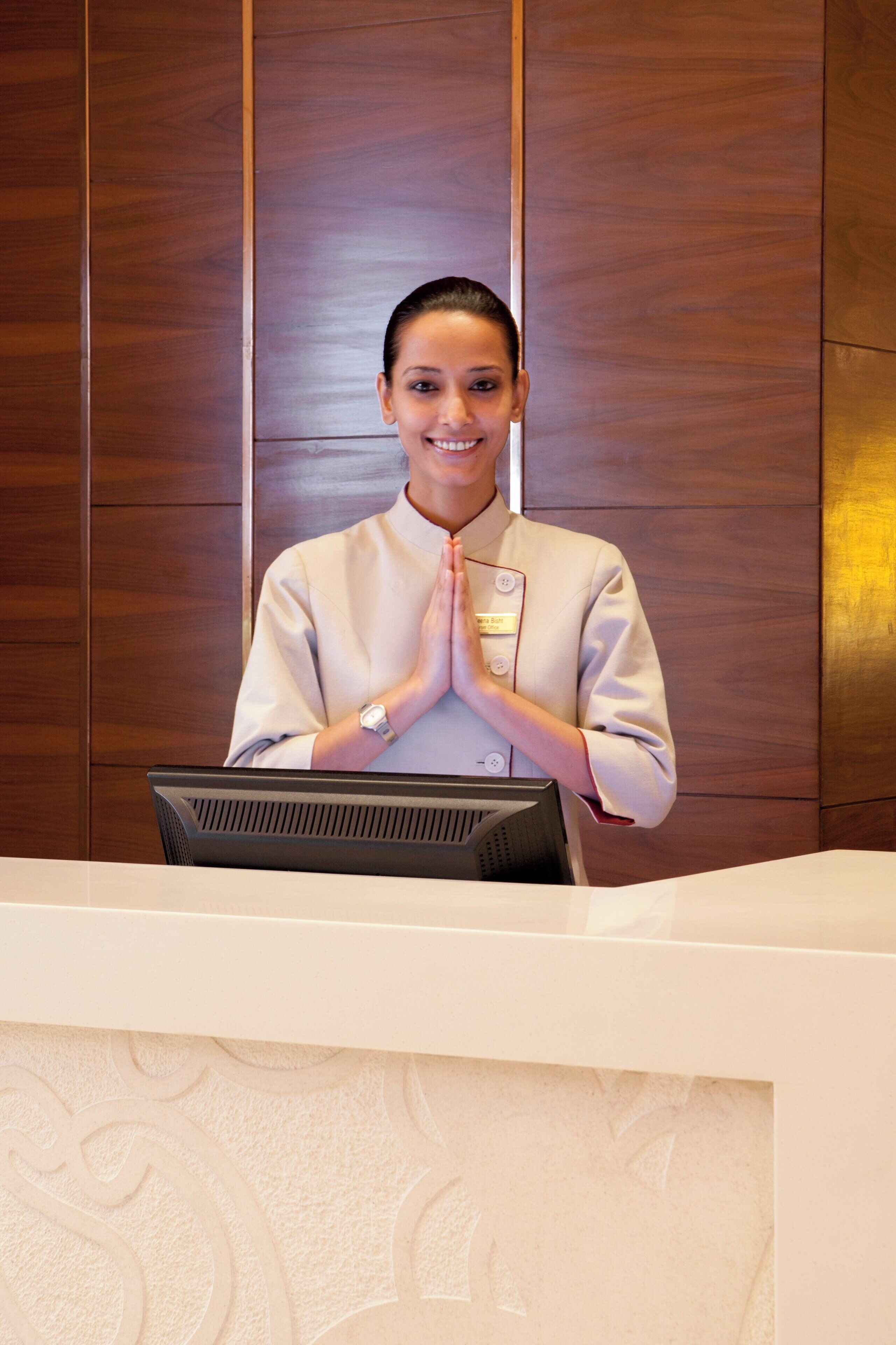 A reception desk with a computer, a name tag, and a person standing behind it.