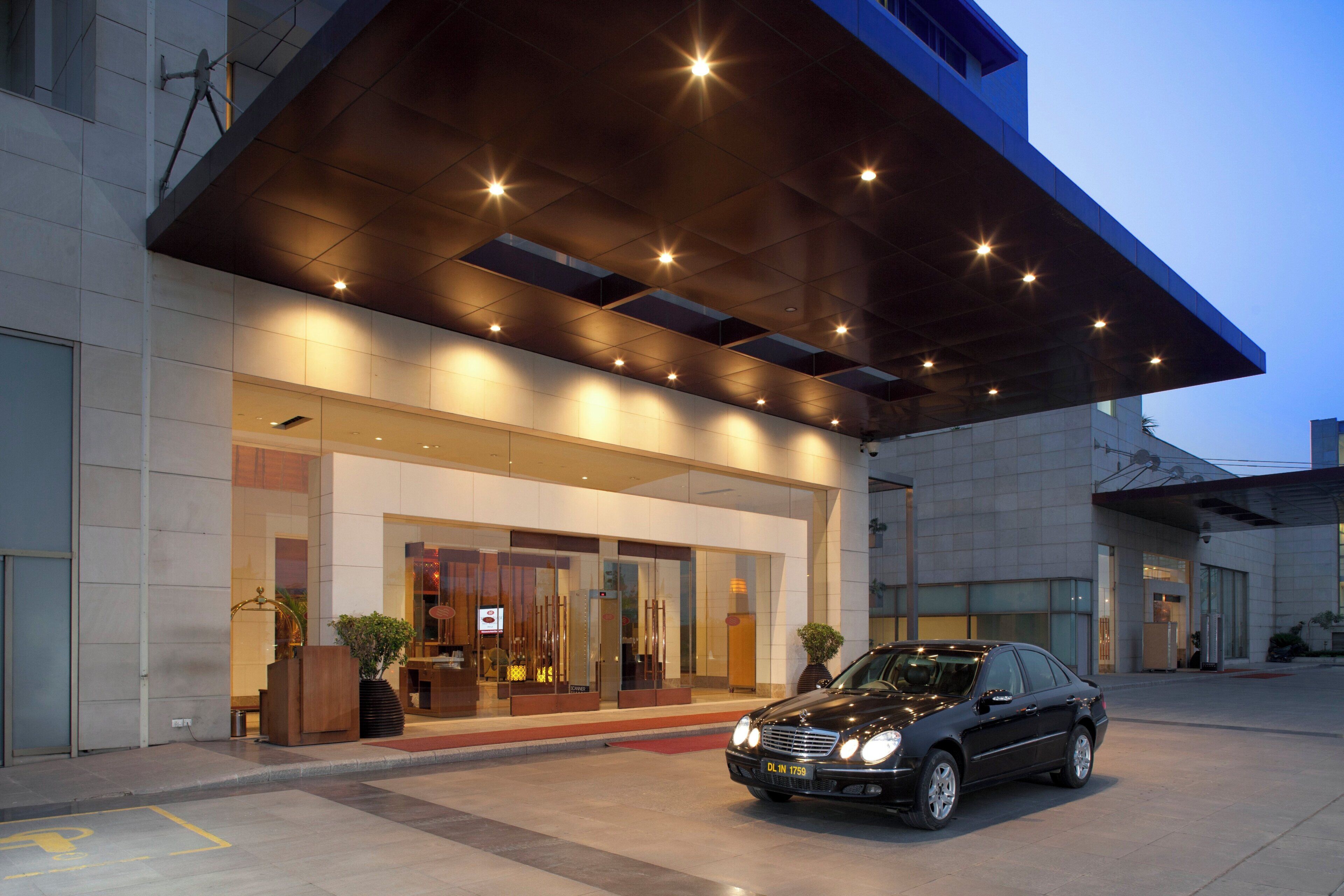 A modern hotel entrance with a covered walkway, a car parked in front, and a clear sky.