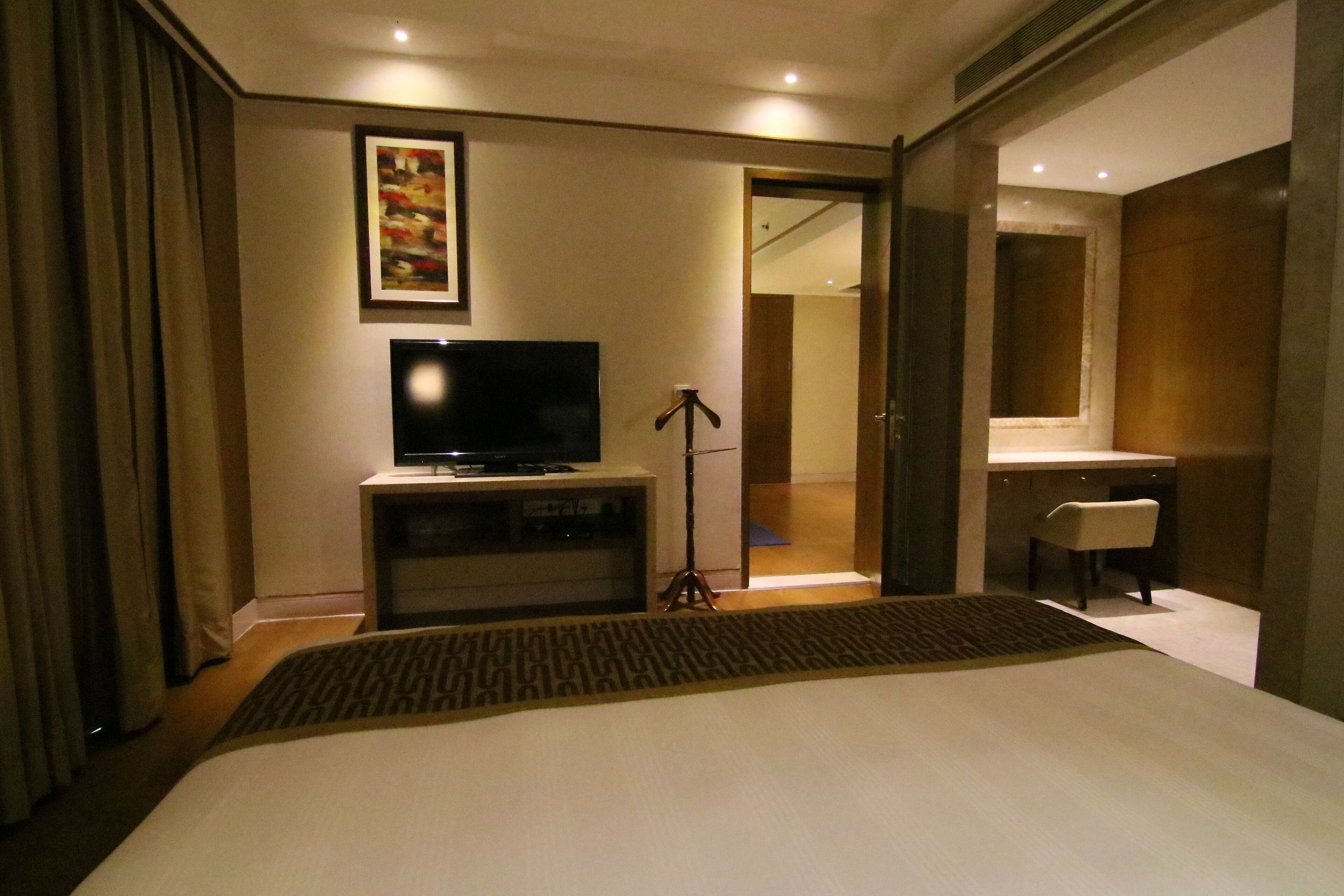 A hotel room with a bed, a television on a stand, a desk with a chair, and a bathroom visible through an open door.
